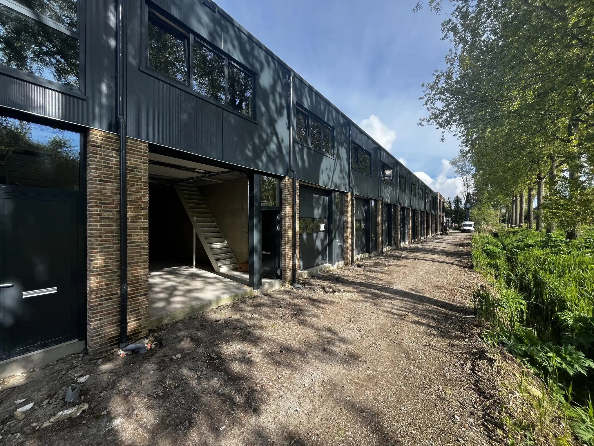 Een rij moderne bedrijfsunits aan de Broekdijk West in aanbouw, met open garages en bouwmateriaal op een onverharde weg.